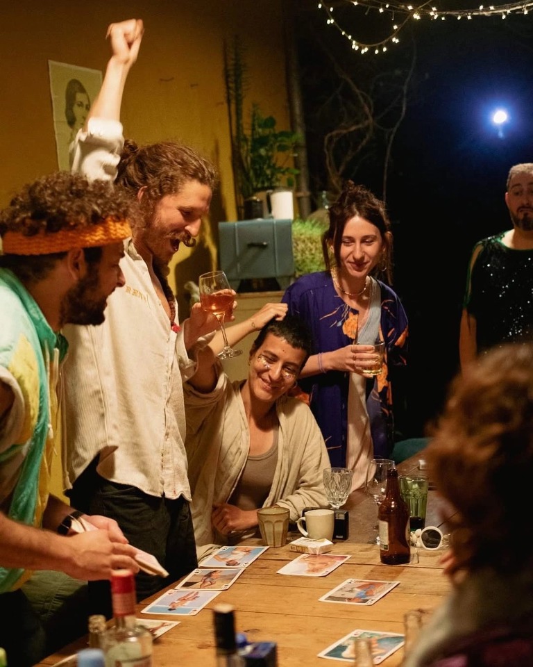 A group of queer friends gathered around a table, talking and sharing a meal.